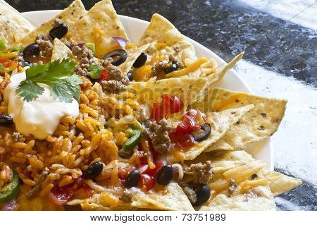 Mexican nachos with sour cream black olives ground beef black beans tomatoes shredded cheese jalapenos rice and cilantro
