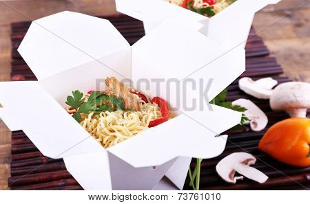 Chinese noodles in takeaway boxes on bamboo mat background