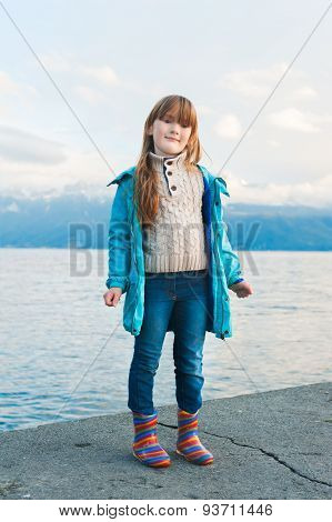Outdoor portrait of a cute little girl resting by the lkae, wearing blue coat