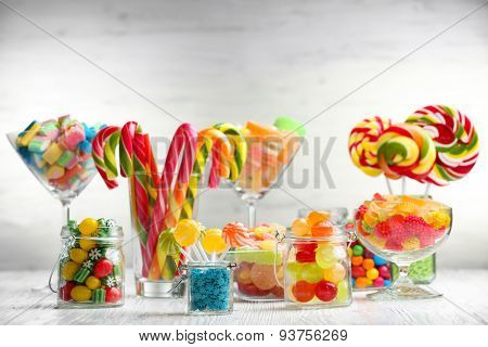 Colorful candies in jars on table on wooden background