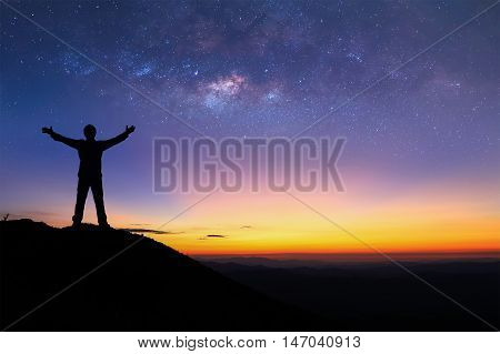 Silhouette of man is standing on top of mountain and spreading hand next to the milky way before sunsire.