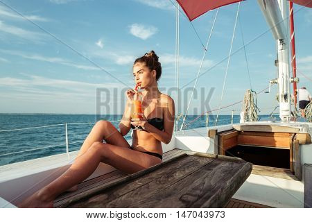 Young beautiful brunette girl drinking cocktail while resting on a yacht