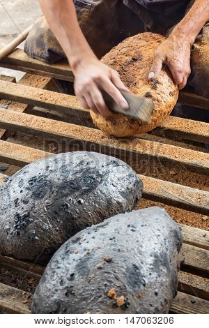 Making bread the traditional way - cleaning the charred crust from an oven baked bread closeup