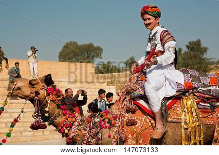 JAISALMER. INDIA - FEB 1, 2015: Young camel rider in colorful dress goes past the tourist crowd of popular Desert Festival on February 1, 2015 in Rajasthan. Every winter Jaisalmer takes the Desert Festival