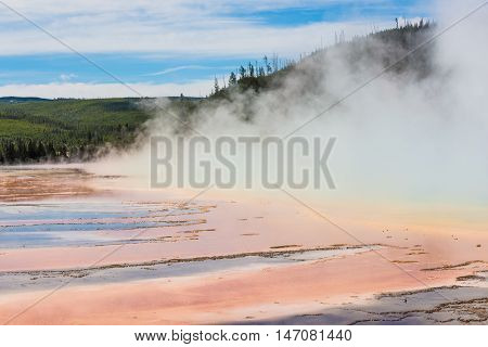 Rising blue steam and mist from hot spring in Midway Geyser basin at Yellowstone National Park with red bacterial patterns