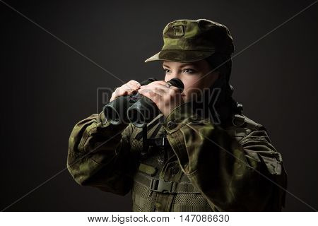 Portrait of unarmed woman with camouflage. Young female soldier observe with binoculars. War military army people concept