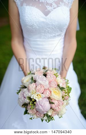 Beautiful bride is holding a wedding colorful bouquet. Beauty of colored flowers. Close-up bunch of florets. Bridal accessories. Female decoration for girl. Details for marriage and for married couple
