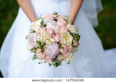 Beautiful bride is holding a wedding colorful bouquet. Beauty of colored flowers. Close-up bunch of florets. Bridal accessories. Female decoration for girl. Details for marriage and for married couple