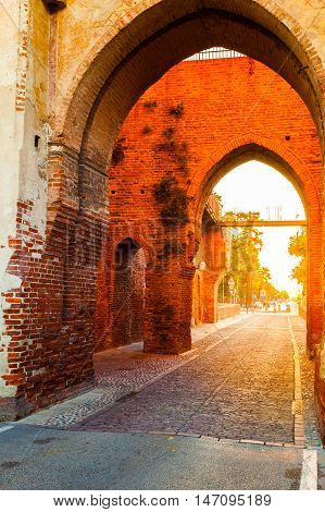 Defensive wall surrounding the small old town of Cittadella in Italy at sunrise. Entrance gate in the wall of red brick illuminated by sun.