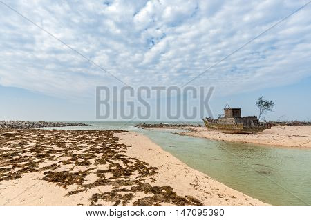An Abandoned Fishing Boat on a beach with dry algae. At Weizhou Island, Guangxi, China.