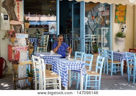 PALEOCHORA, CRETE, GREECE - JUNE 2016: Man sitting at traditional Greek tavern at Paleochora town on Crete island