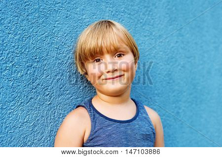 Close up portrait of adorable little 5 year old boy standing against bright blue wall