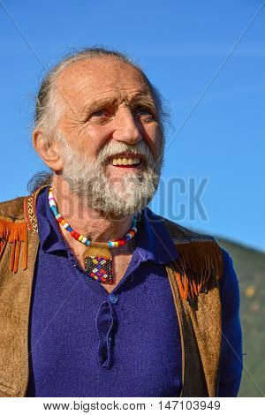 Porrait of impressive elderly man dressed in hippie style against blue sky in a bright sunny autumn day