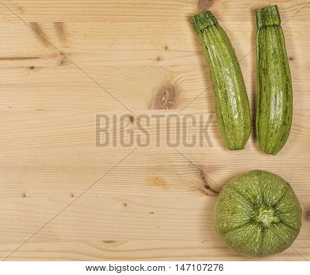 Composition of green courgette (zucchini) on a wooden table, two common and one zucchini Di Nizza