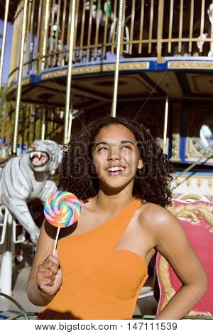 cool real modern teenage girl with candy near carousels at amusement park walking, having fun