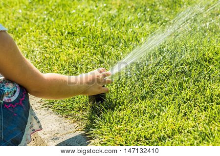 Little girl holding during irrigation, spray on the grass