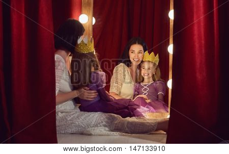 Cute little actress. Young mother and her daughter child girl in Princess costume on the background of theatrical scenes and mirrors.