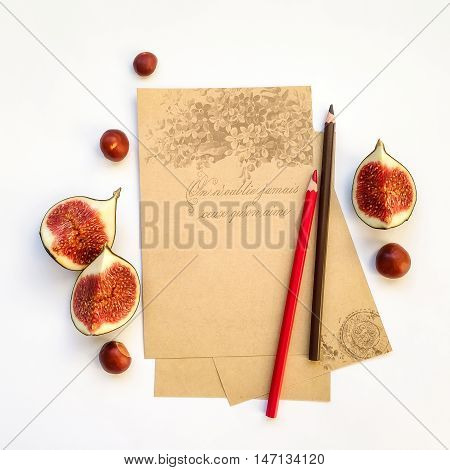 Decorative composition of empty old paper sheets with pencils fig fruits and chestnuts on white background. Flat lay top view writing or painting concept