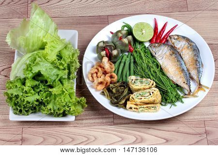 Ready side dish served as deep fired mackarelss,vegetable omelet,crispy pork rind,pickle lettuce,halve green lemon,red chili and boiled of eggplant,lentils,acacia  on wood. Side view