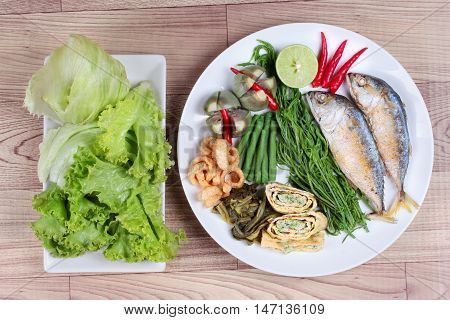 Ready side dish served as deep fired mackarelss,vegetable omelet,crispy pork rind,pickle lettuce,halve green lemon,red chili and boiled of eggplant,lentils,acacia on wood.Top view