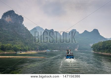 Xingping China - October 20 2013: A tourist boats travels the magnificent scenic route along the Li river from Guilin to Yangshou in cloudy weather.
