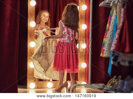 Cute little fashionista. Happy child girl try on outfits and mom's shoes looking at mirror.