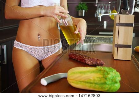 Woman in white underwear holds oil near table in kitchen, noface