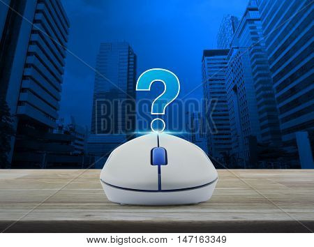 Wireless computer mouse with question mark sign icon on wooden table over city tower background Customer support concept