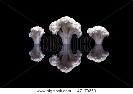 Three white cauliflowers on glossy black background