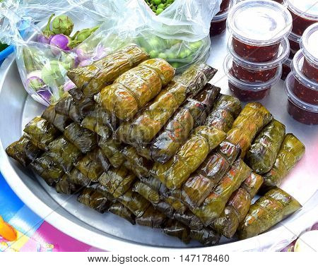 tray with stack of rolled mashed banana and rice pasteries, wrapped in banana leaves, Ranot water market