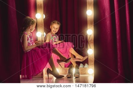 Cute little fashionista. Happy child girl try on outfits and mom's shoes looking at mirror.