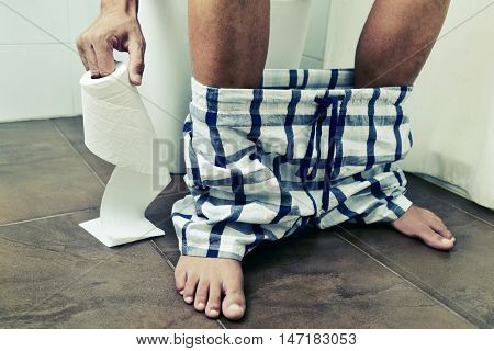 detail of a young caucasian man in the toilet sitting in the toilet, with a roll of toilet paper in his hand