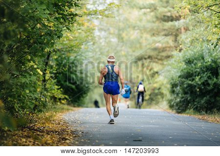 back oldest male runner marathon running in autumn Park. yellow leaves on ground