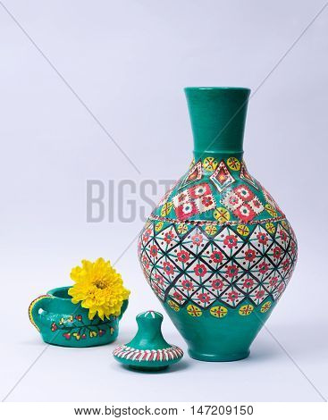 Still life of green ornate pottery vase lid green pottery cup and yellow flower on white background