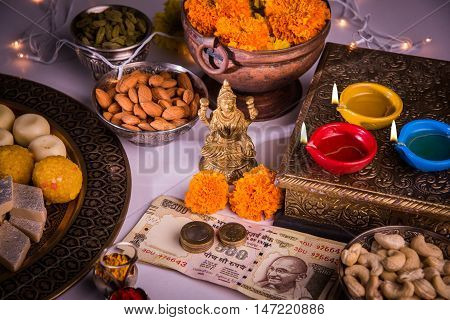 oil lamp or diya with crackers, sweet or mithai, dry fruits, indian currency notes, marigold flower and statue of Goddess Laxmi on diwali night while laxmi pujan or pooja
