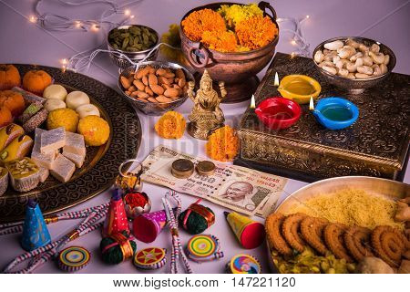 oil lamp or diya with crackers, sweet or mithai, dry fruits, indian currency notes, marigold flower and statue of Goddess Laxmi on diwali night while laxmi pujan or pooja