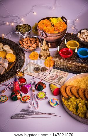 oil lamp or diya with crackers, sweet or mithai, dry fruits, indian currency notes, marigold flower and statue of Goddess Laxmi on diwali night while laxmi pujan or pooja