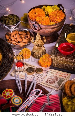 oil lamp or diya with crackers, sweet or mithai, dry fruits, indian currency notes, marigold flower and statue of Goddess Laxmi on diwali night while laxmi pujan or pooja