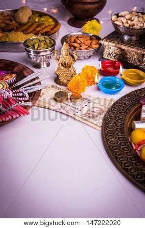 oil lamp or diya with crackers, sweet or mithai, dry fruits, indian currency notes, marigold flower and statue of Goddess Laxmi on diwali night while laxmi pujan or pooja