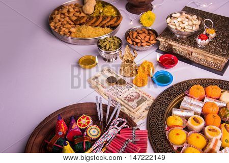 oil lamp or diya with crackers, sweet or mithai, dry fruits, indian currency notes, marigold flower and statue of Goddess Laxmi on diwali night while laxmi pujan or pooja