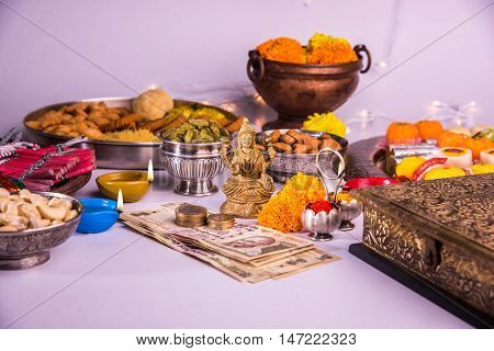 oil lamp or diya with crackers, sweet or mithai, dry fruits, indian currency notes, marigold flower and statue of Goddess Laxmi on diwali night while laxmi pujan or pooja