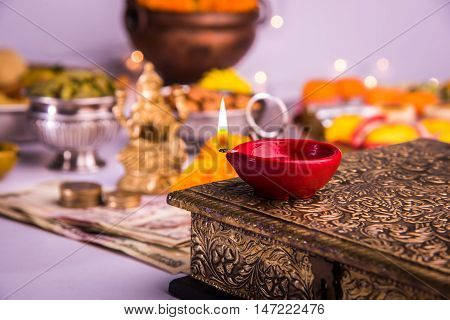 oil lamp or diya with crackers, sweet or mithai, dry fruits, indian currency notes, marigold flower and statue of Goddess Laxmi on diwali night while laxmi pujan or pooja