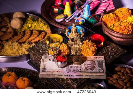 oil lamp or diya with crackers, sweet or mithai, dry fruits, indian currency notes, marigold flower and statue of Goddess Laxmi on diwali night while laxmi pujan or pooja