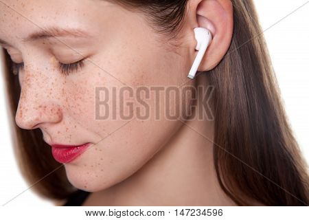 Young beautiful woman with freckles and wireless earphones on her ears. studio shot.
