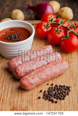 Raw beef sausages with tomatoes and sause on kitchen wooden board. Potatoes and pepper