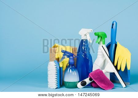 Cleaning concept - mixed detergents and cleaning accessories isolated on blue seamless background.