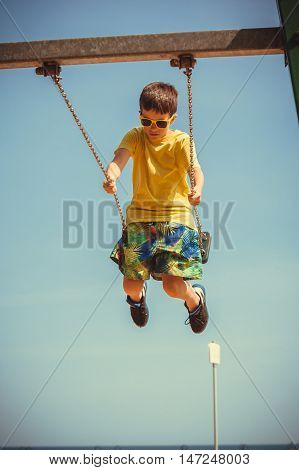 Rest and relax for children. Little boy in sunglasses resting swinging outdoor. Adorable child having fun playing in playground.
