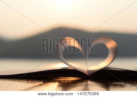 close up heart shape from paper book at sunset with light reflection on a water surface (vintage background)