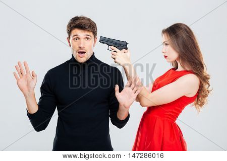 Beautiful young woman standing and threatening with gun to scared young man