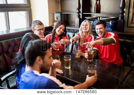 people, leisure and sport concept - happy friends or football fans drinking beer and watching soccer game or match at bar or pub, supporting two teams with different shirt color
